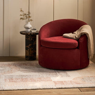Red armchair with a beige blanket on a wooden floor in a room with a side table and decorative elements.