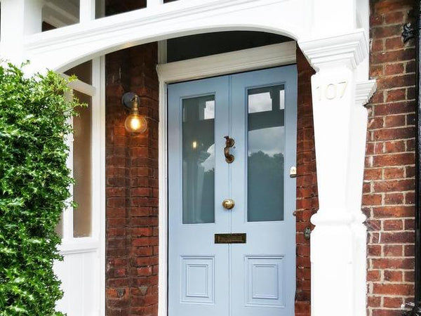 Globe wall light placed on a front porch beside a blue door. 