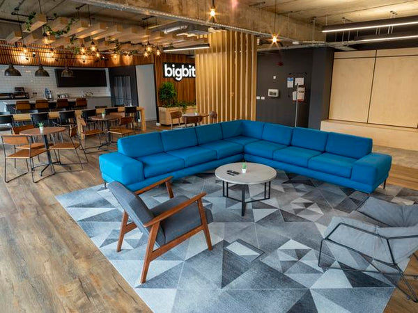 A recreational space in an office with sofas, chairs, a kitchen area and pendant lights. 