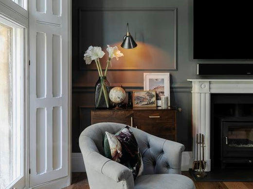 A cone wall light shining in a living room over a side table and chair. 