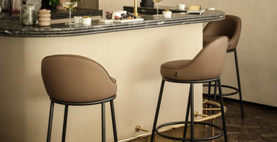 Warm living room with a brown corduroy sofa, patterned throw, and blue cushion, paired with two cube pouffes, a soft patterned rug, and two stone pedestal coffee tables styled with candles, books, and a glass vase of flowers.