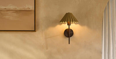 Ceramic hallway wall light with a pleated bronze shade, casting warm ambient lighting against a textured wall.