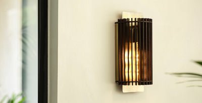 Modern and contemporary wall light with a sleek brass cage design, casting a warm glow against a neutral wall.