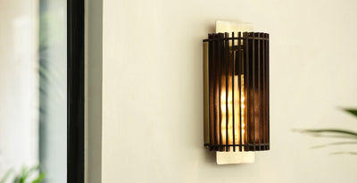 Modern and contemporary wall light with a sleek brass cage design, casting a warm glow against a neutral wall.