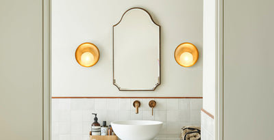 Modern bathroom with twin brass wall lights flanking a vintage mirror above a wooden vanity unit with a white countertop basin.
