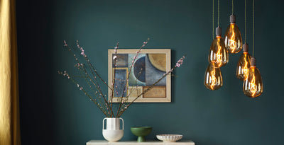 Cluster of amber LED decorative light bulbs with exposed filaments, creating a warm glow against a deep green wall.