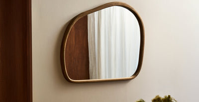 Organic-shaped wall mirror with a natural wooden frame, styled against a neutral interior wall.