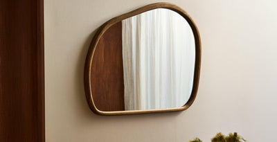 Organic-shaped wall mirror with a natural wooden frame, styled against a neutral interior wall.