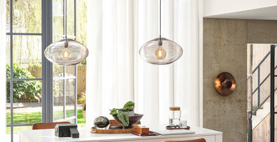 Modern and contemporary ceiling lights featuring smoked glass pendant shades with exposed bulbs, styled above a bright dining space with a copper wall light.