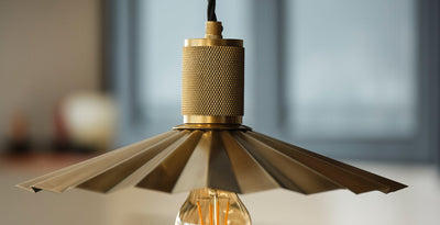 Close-up of a brass pendant light with a knurled bulb holder and pleated metal shade, showcasing modern industrial design.