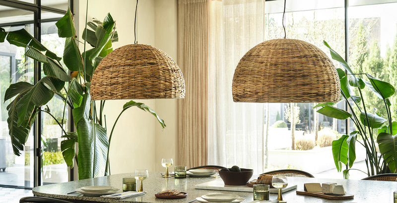 Dining room with two large dome-shaped sea grass pendant lights hanging above a modern table, styled with greenery and natural light.