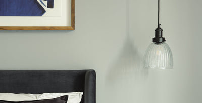 Matt black light pendant with ribbed glass shade, styled as bedside lighting for a modern bedroom.