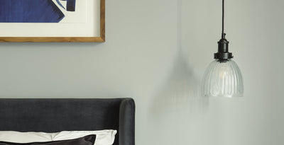 Matt black light pendant with ribbed glass shade, styled as bedside lighting for a modern bedroom.