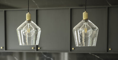 Kitchen island lighting with clear glass pendant lights and brass fittings, adding a modern touch to a sleek dark cabinetry backdrop.