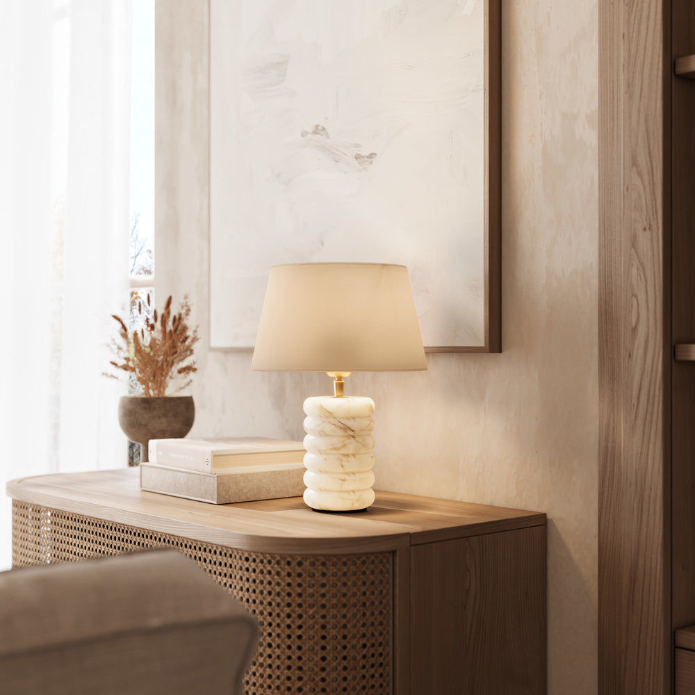 Alabaster table lamp with dual lighting illuminated featuring a light natural cotton medium empire shade