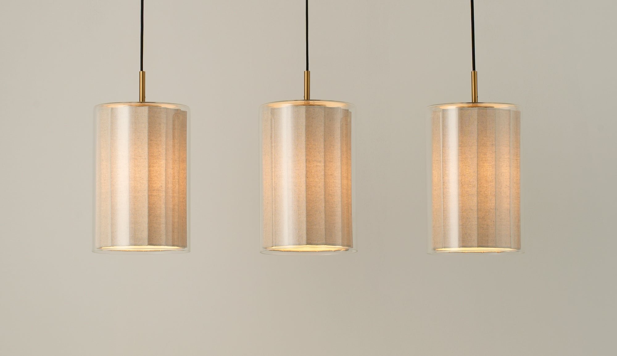 Bude Cylinder 3 Wire Cluster Pendant Light with Linen  and Clear Glass shades lit up, close up of the three shades 