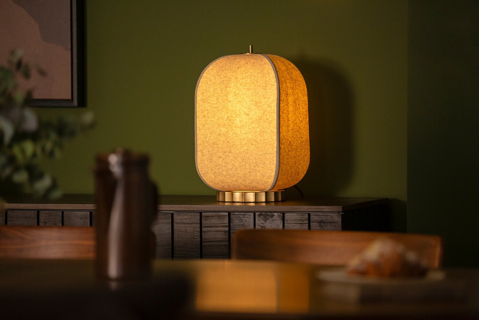 Table lamp with a warm glow on a wooden surface against a green wall.