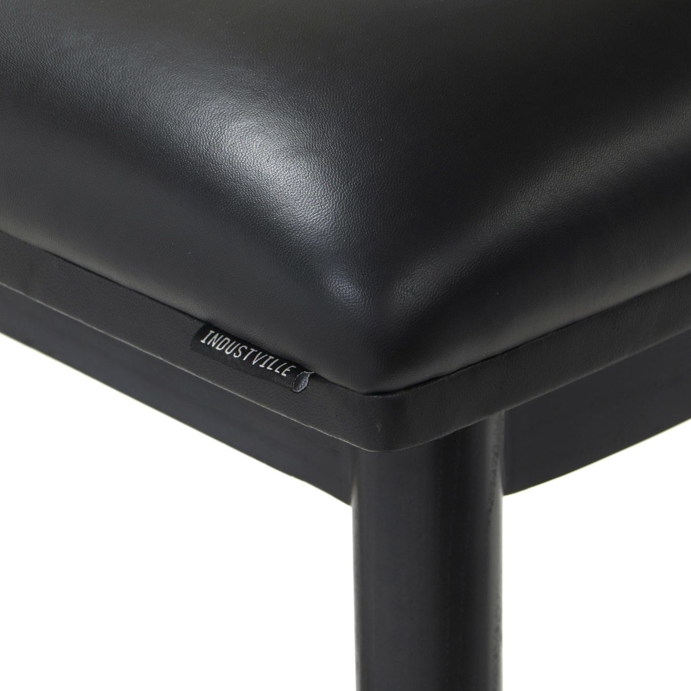 Close-up of the black leather seat cushion of a bar stool, displaying the soft texture and the Industville brand label