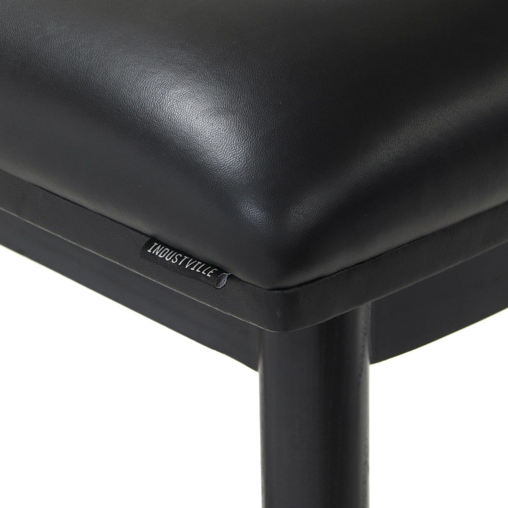Close-up of the black soft leather seat on a counter height stool, showing the Industville brand label and the fine texture.