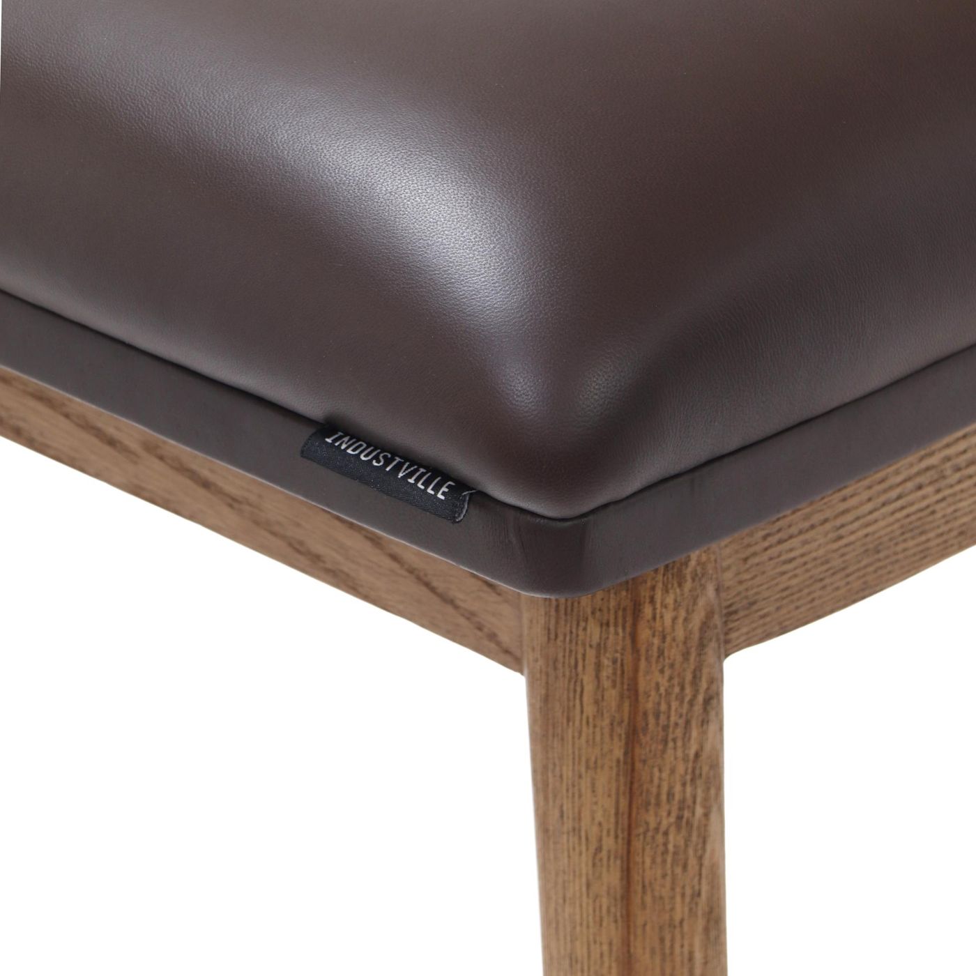 Close up of the brown soft leather seat on a counter height stool with natural ash wood legs, featuring the Industville brand label.