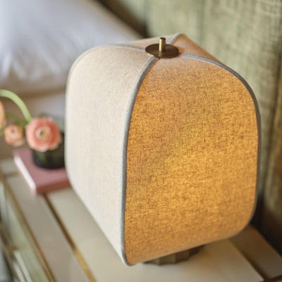 Bloxham Rectangular Table Lamp in Natural Fabric finish lit up next to a bed